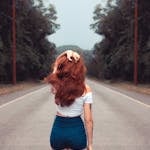 Red-haired woman in jean shorts walking down a forest road, showcasing style and freedom.